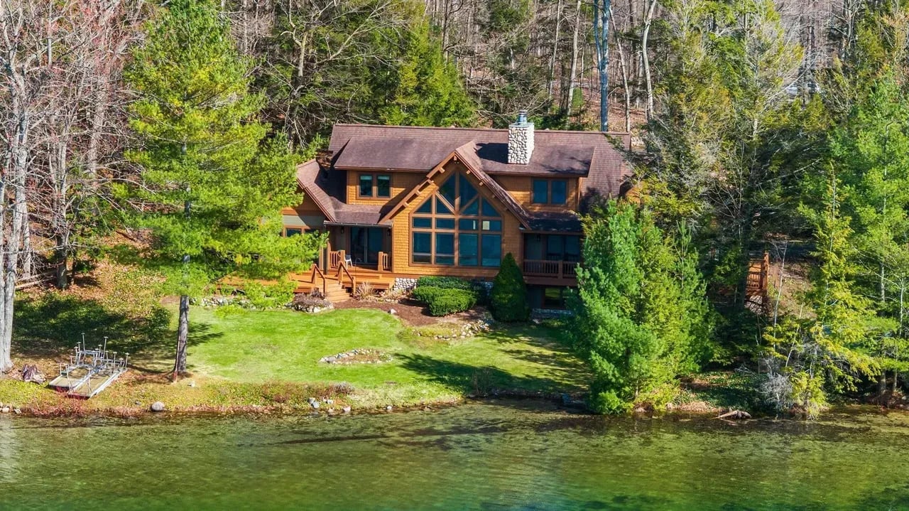 Timber-frame lakefront home with a wall of windows, wooded hillside behind and clear green water in front, Northern Michigan