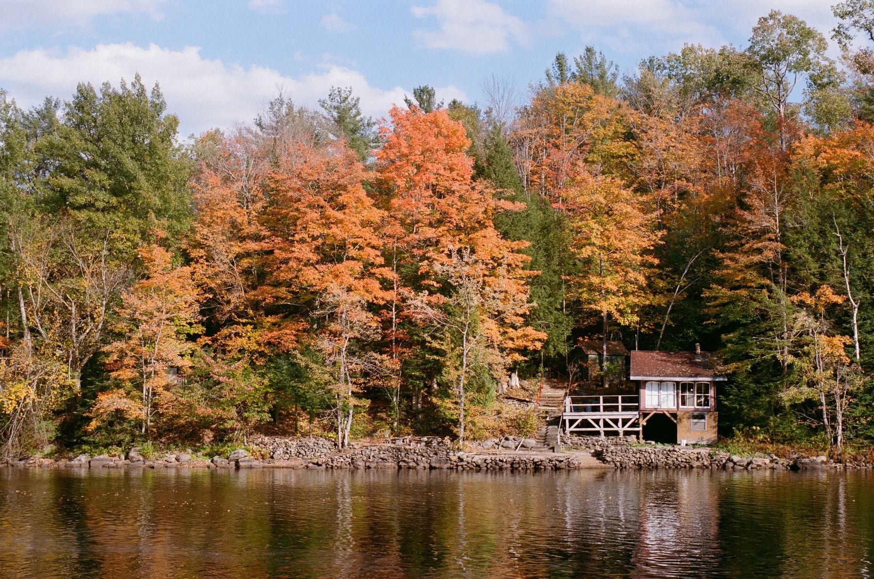 Small cabin on a rocky lakeshore beneath maples in full autumn color